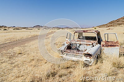 Wreck of abandoned classic car in between dry grass next to dirt road in Damaraland, Namibia, Southern Africa Stock Photo