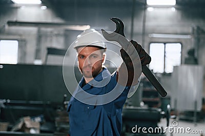 Wrench in the hand. Factory worker in blue uniform is indoors Stock Photo