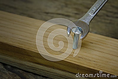 wrench screwing nut a furniture screw into a wooden plank, The effort wrong of tools as a fail concept Stock Photo