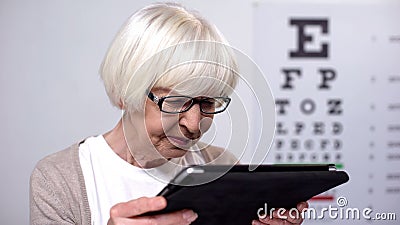 Wrinkled elderly woman holding tab and trying to read, unhappy with poor sight Stock Photo