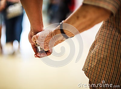 Wrinkled elderly woman`s hand holding to young man`s hand, walking in shopping mall.Family Relation, Health, Help, Support concept Stock Photo