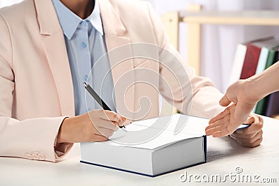 Writer signing autograph in book at table, Stock Photo