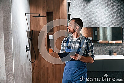 Writes down information in a notebook. Plumber in blue uniform is at work in the bathroom Stock Photo