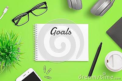 Writing goals on notepad page concept. Green office desk with smart phone, glasses, folder, coffee, plant Stock Photo