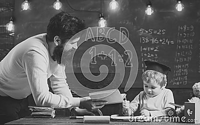 Wunderkind and genius concept. Father, teacher reading book, teaching kid, son, chalkboard on background. Boy child in Stock Photo