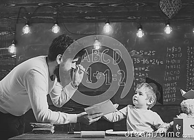 Wunderkind and genius concept. Father, teacher reading book, teaching kid, son, chalkboard on background. Dad wants to Stock Photo
