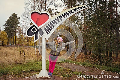 'I love Michurinskoye village' written on a pole and happy patriotic russian girl stretching her arms against Stock Photo