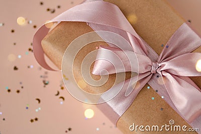 Xmas gift package in kraft paper with pink ribbon on trendy natural beige background with glitter. Zero waste pack Stock Photo
