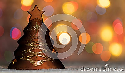 Xmas tree shaped candle holder standing in snow, with christmas tree lights, bokeh background and copy space Stock Photo