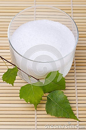 Xylitol birch sugar in glass bowl with birch leaves on bamboo mat Stock Photo