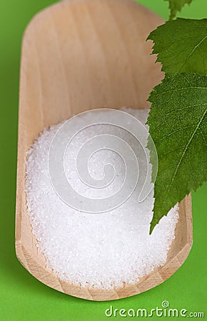 Xylitol birch sugar on wooden scoop over green Stock Photo