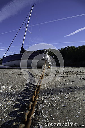 Yacht boat on a sandy beach tethered with a rusty chain Stock Photo