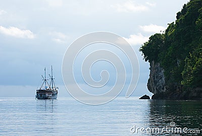Yacht sailing next to rocky island Stock Photo