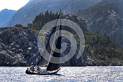 A yacht sailing in strong wind in Aegean sea and passing by the rocks and cruising to a bay Editorial Stock Photo