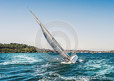 A Yacht tilting, heeling in the water it has a large silver grey sail and is cutting through the blue water of Sydney harbour. Editorial Stock Photo