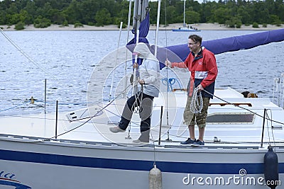 Yachtsmen stand on a deck of sailing yacht with ropes in hands ready to moor to a berth Editorial Stock Photo