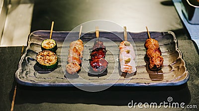 Yakitori Japanese-Style Grilled Chicken Skewers with chicken, internal organ and cucumber served on black stone plate Stock Photo