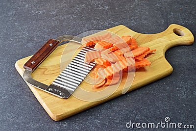 Yams, sweet potato cut in pieces with a special knife with ribs on a cutting board on a grey background. Cooking step by Stock Photo