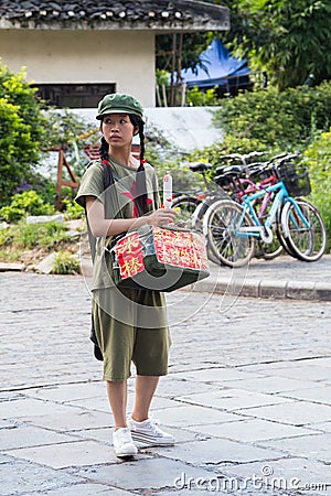 Yangshuo, China - circa July 2015: Chinese young pioneer girl sells food or souvenirs on the streets of tourist town Yangshuo on t Editorial Stock Photo