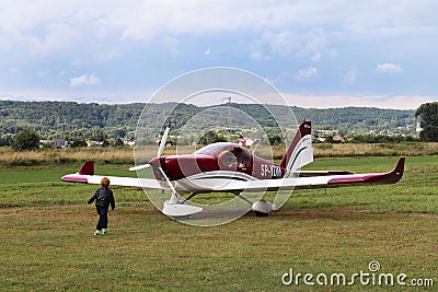 Yaslo, Poland - july 3 2018: The little boy runs along the grassy airfield to the light two-seater tuppovintovom airplane. Raising Editorial Stock Photo