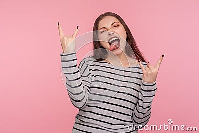 Yeah, awesome ! Portrait of excited rocker woman in striped sweatshirt showing rock and roll hand gesture Stock Photo