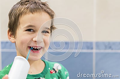 A 5-year-old boy at home washes his teeth with an oral irrigator. Little boy cleaning teeth with oral irrigator. Dental Care Stock Photo