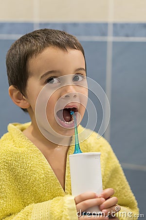 A 3-year-old boy at home washes his teeth with an oral irrigator. Little boy cleaning teeth with oral irrigator. Dental Care Stock Photo