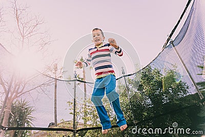 5 year old boy jumping on a trampoline exercising in the backyard of his house, enjoying the spring with gesture of happiness and Stock Photo