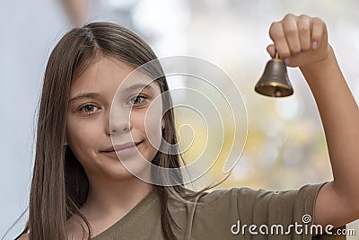 An 11-year-old girl rings a bell on a blurry neutral background. Stock Photo