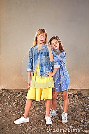 10-year-old girls of different races, standing against a gray wall, hug each other and look at the camera. Stock Photo