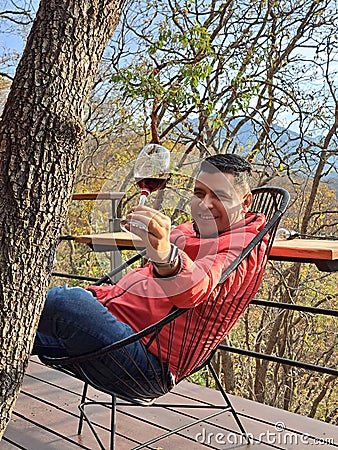 40-year-old Latino man drinks wine on the terrace of his cabin in the woods relaxes in his free time on weekend vacations Stock Photo