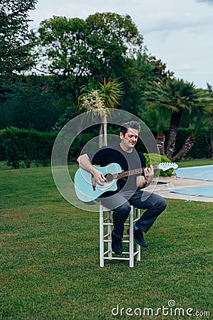 40-50 year old man with a tupe and gray hair playing an acoustic guitar in a garden Stock Photo