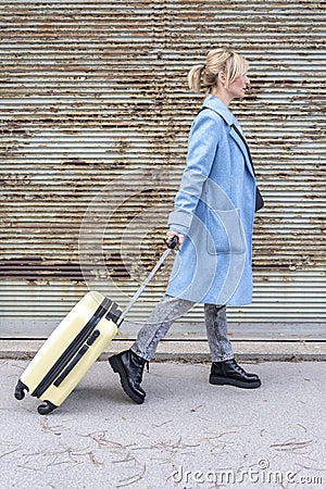 A 40-45-year-old woman pulls a suitcase on a textured background of rusty garage shutters Stock Photo