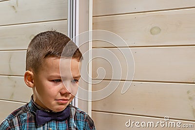 A 4 years old boy in a blue clerical shirt is crying on a light wooden background Stock Photo