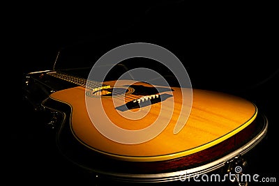 Yellow acoustic guitar lying in a hard case in the dark on a black background. Wooden stringed instrument illuminated by Stock Photo