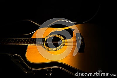 Yellow acoustic guitar lying in a hard case in the dark on a black background. Wooden stringed instrument illuminated by Stock Photo