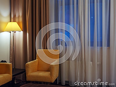 A yellow armchair next to a luminous floor lamp in the corner of the room near the window. Fragment of the interior of a Stock Photo