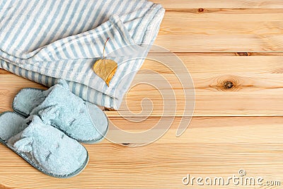 Yellow autumn leaf over striped fuzzy blanket and funny cat face blue slippers over natural wood surface. Warm fleece bedding and Stock Photo