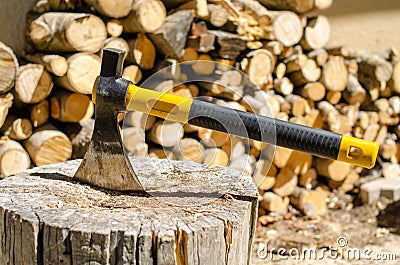 Axe with a piece of wood near a stack of logs Stock Photo