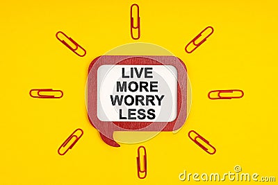 On a yellow background, paper clips and a mental plaque with the inscription - Live More Worry Less Stock Photo