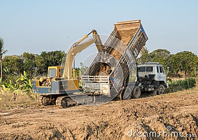 Yellow backhoe digging soil fill in rear truck Stock Photo
