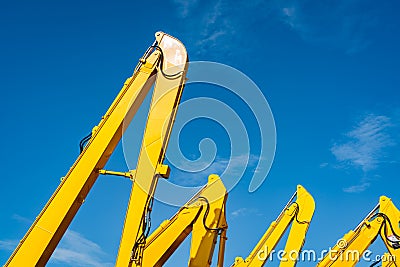 Yellow backhoe with hydraulic piston arm against clear blue sky. Heavy machine for excavation in construction site. Hydraulic mach Stock Photo