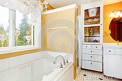 Yellow bathroom with white storage combination and elegant chandelier. Stock Photo