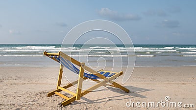 An yellow beach chair rests on the white sand of the beach and B Stock Photo