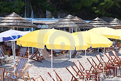 Yellow beach umbrellas and chaise for relax and comfort on sea coast. Happy summer vacations and tourism concept. Paid service on Stock Photo