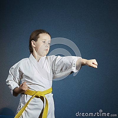 With a yellow belt, sportswoman is beating punch hand on a dark blue background Stock Photo