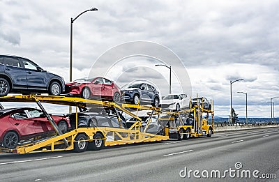 Yellow big rig car hauler semi truck transporting cars on two level hydraulic semi trailer driving on the wide highway road Stock Photo