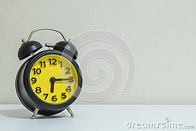 Closeup yellow and black alarm clock for decorate show a quarter past six or 6:15 a.m.on white wood desk and cream wallpaper textu Stock Photo