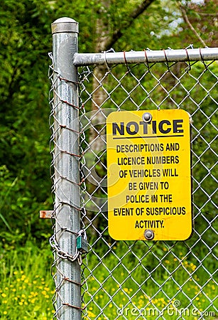 Yellow and black neighborhood crime warning sign posted on chain link fence. Editorial Stock Photo