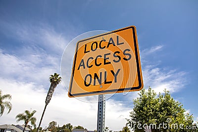 Yellow and black square road sign in neighborhood reading Local Access Only against a blue sky with palm trees Stock Photo